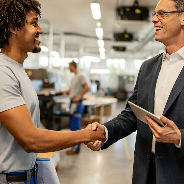 happy engineer greeting african american worker in industrial building.
